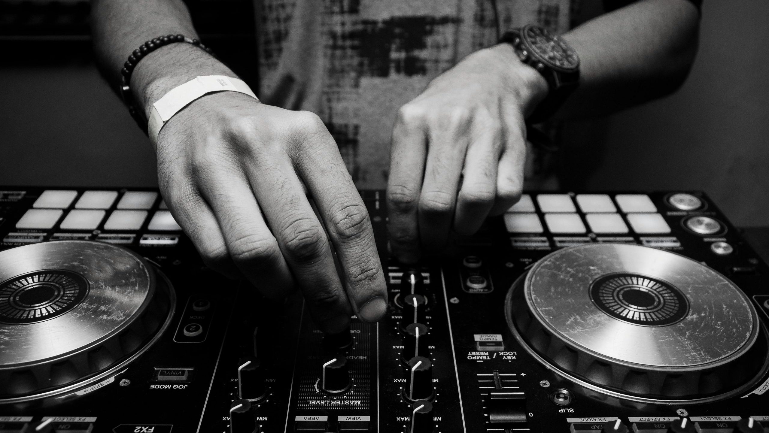 Close-up of a DJ's hands adjusting controls on a mixer in monochrome.